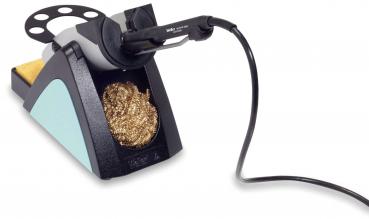 The image displays a soldering tool on a stable base. It features a holder for the soldering iron and below that, a gold-colored cleaning spiral. A sponge is also included.
