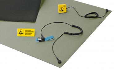 The image shows a green ESD work mat. Attached to the mat are a yellow safety symbol, a blue grounding clip, and a cable with a plug.