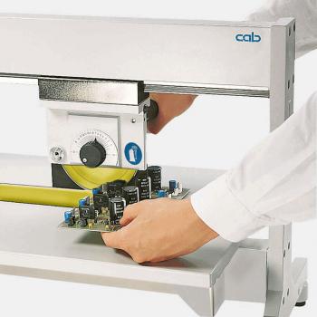 Das Bild zeigt eine Person, die mit einer Maschine ein elektronisches Bauteil bearbeitet. Die Maschine hat einen großen gelben Schneidekopf und ein verstellbares Bedienfeld.