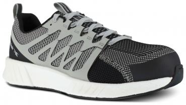 Der Schuh ist sportlich, größtenteils grau mit roten Akzenten. Er hat ein atmungsaktives Netzmaterial, eine massive Zehenkappe und eine weiße, strukturierte Sohle. Die Schnürsenkel sind rot.