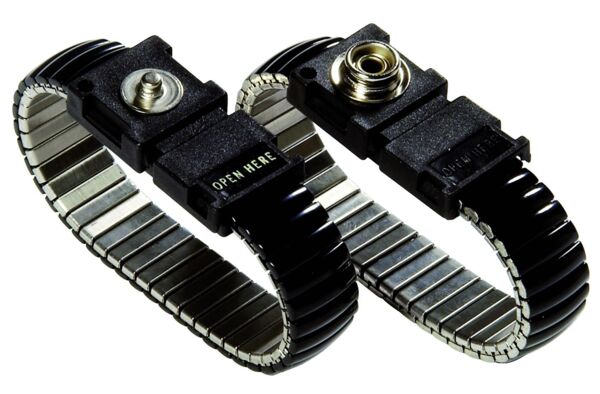 The image shows a black, metallic bracelet with a flexible, springy structure. In the center, there is a rectangular clasp marked with the inscription 