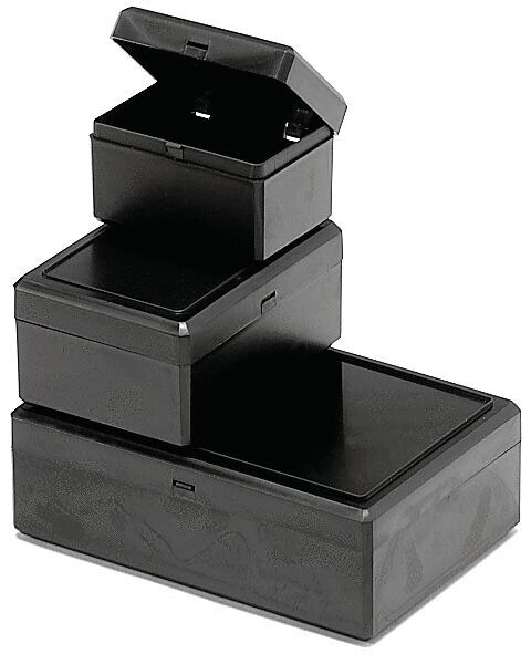 Es handelt sich um eine schwarze, rechteckige Box mit einem flachen Deckel. Die Kanten sind leicht abgerundet, und eine schmale Öffnung an der Vorderseite ermöglicht das Einlegen von Objekten.