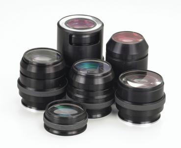 The image displays multiple black camera lenses in various sizes and shapes. Some lenses feature a shiny, transparent surface, while others are matte. They are artfully arranged.