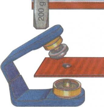 The image shows a lever device with a grey weight of 200 g. A screw with a roller presses on a red metal piece to secure it.