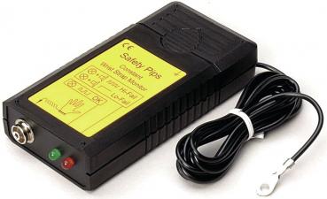 The image shows a black device with yellow lettering, two buttons, and a connector. Next to it lies a black plug with two prongs and a short cable.