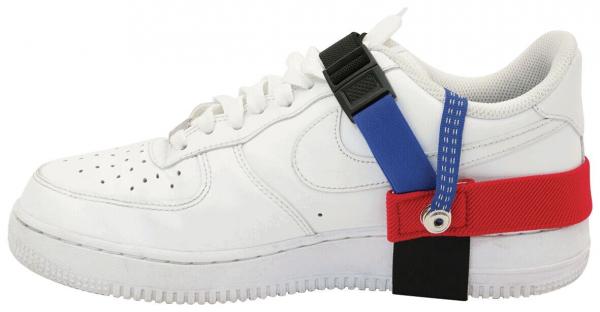 Das Bild zeigt einen weißen Sneaker mit verschiedenen farbigen Riemen: rot, blau und schwarz, die seitlich am Schuh befestigt sind. Der Schuh hat eine klassische Sneakerform mit Schnürsenkeln.
