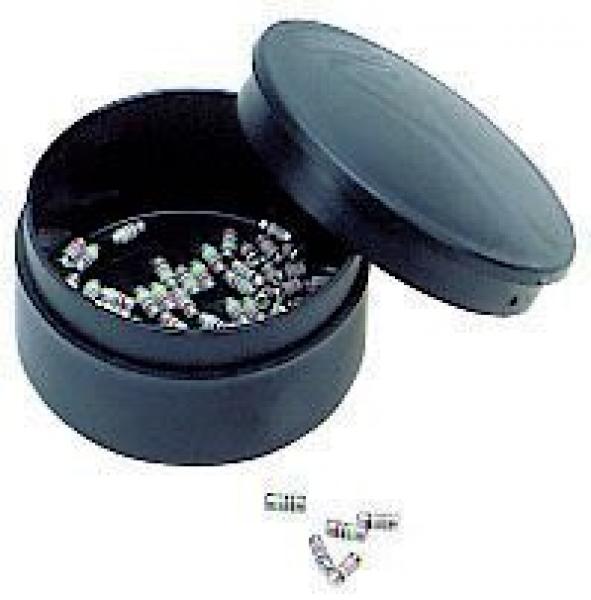 The image shows a round, black can with a slightly raised lid. The can is open and contains several small, silver parts scattered on the bottom of the can. Some are lying outside the can.
