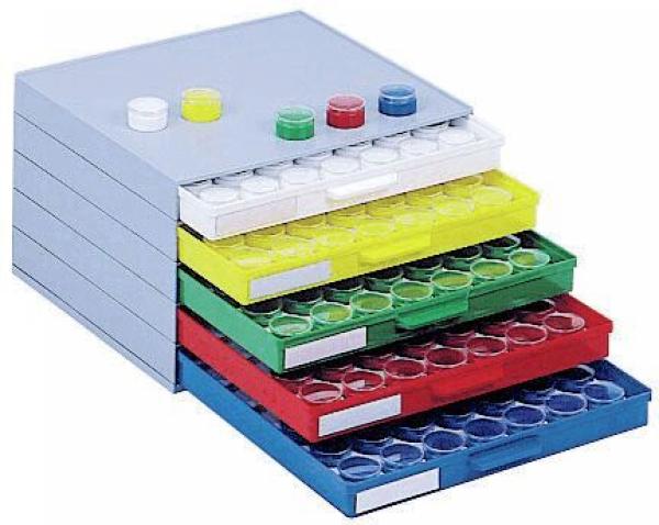 Das Bild zeigt eine stapelbare Box mit fünf Schubladen in verschiedenen Farben ? Grau, Gelb, Grün, Rot und Blau. Jede Schublade hat Öffnungen für kleine, runde Behälter.