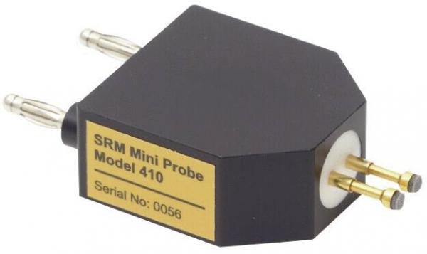 Das Bild zeigt einen kleinen, sechseckigen, schwarzen Mini-Sensor mit zwei Metallstiften an der Oberseite und einem runden Anschluss an der Unterseite. Eine goldene Plakette trägt die Aufschrift ?SRM Mini Probe Model 410?.