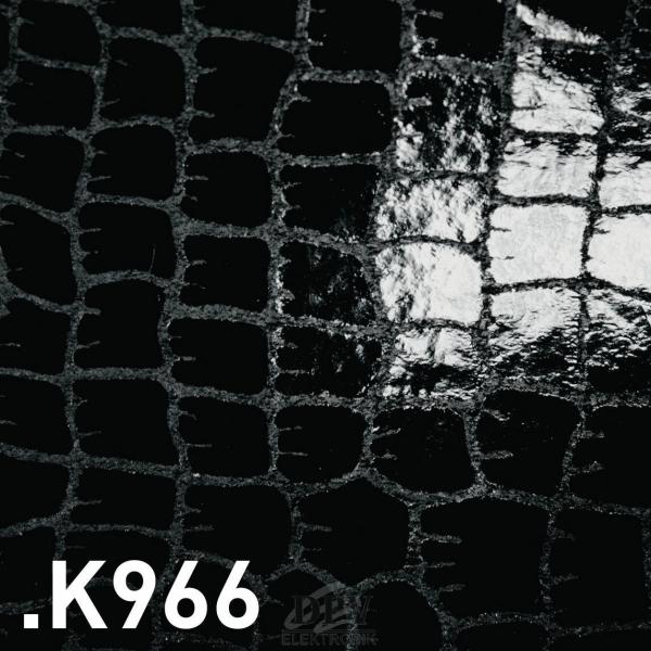 The image displays a black, shiny surface with a pattern of rectangular scales reminiscent of crocodile leather. The texture is irregular and slightly raised.