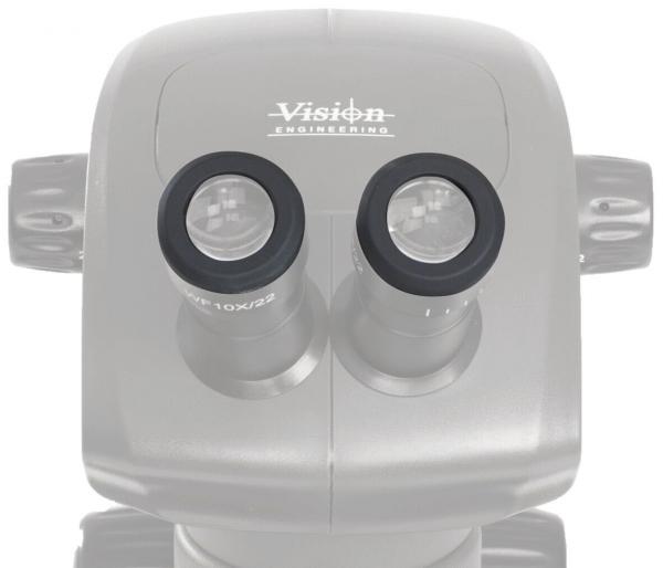 Das Bild zeigt ein Mikroskop mit zwei runden Okularen. Die Oberfläche ist glatt und oval. Oben steht der Schriftzug "Vision Engineering". Es ist ein technisches Gerät zur Vergrößerung von Objekten.