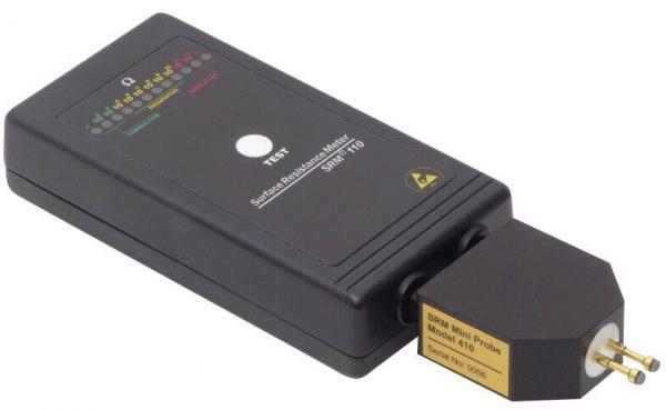 Das Bild zeigt ein schwarzes elektrisches Prüfgerät in rechteckiger Form mit einem Stecker. Oben sind bunte LEDs und ein gedrückter Knopf sichtbar. Es dient zur Überprüfung elektrischer Anschlüsse.