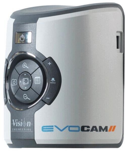The image shows a compact, rectangular camera in silver with a shiny casing. On the front, there is a main button and several control knobs arranged in a circular layout.