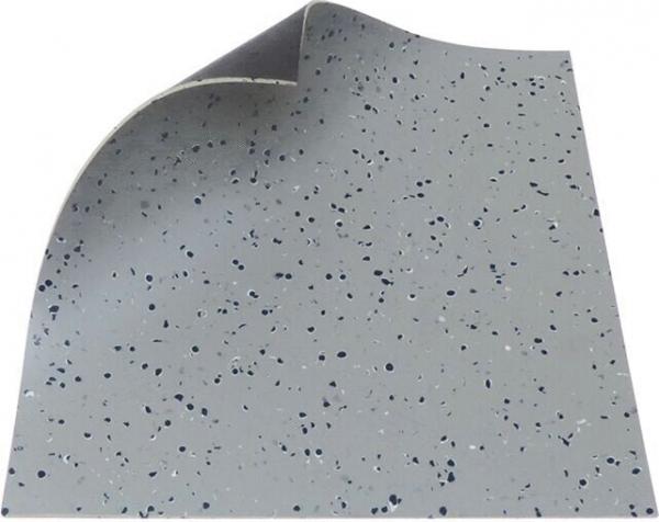 The image displays a piece of light gray flooring with small, dark spots. One corner is slightly bent, revealing the texture of the material.
