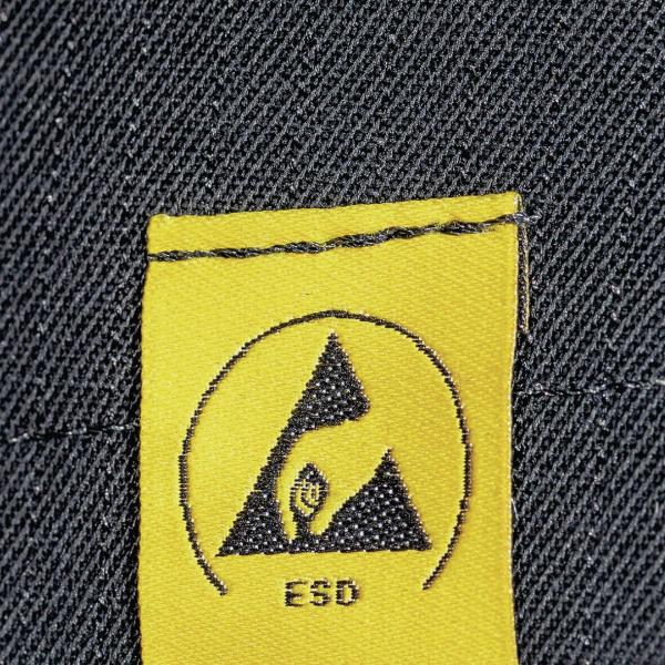 Das Bild zeigt ein gelbes Etikett mit einem schwarzen Symbol in Form eines Dreiecks und einer Hand. Darunter steht "ESD". Der Hintergrund ist aus dunkler Denim-Textur.