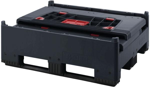 Das Bild zeigt eine schwarze Verpackung oder einen Behälter mit rotem Detail. Er hat eine flache, rechteckige Form, ist stabil und hat Öffnungen an den Seiten, die das Tragen erleichtern.
