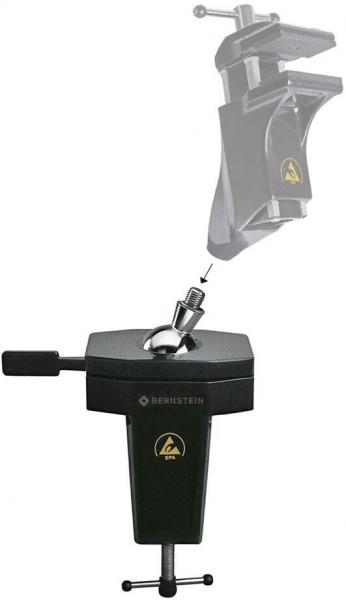 The image shows a black holding device with an adjustable clamp on top. It is square, has a handle, and a screw for attachment. A movable arm is visible on top.