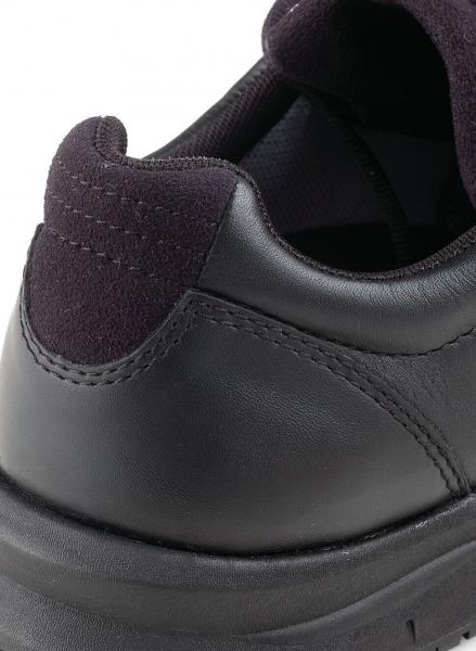 Das Bild zeigt die Rückseite eines schwarzen Sneakers. Der Schuh besteht aus einer glatten Lederoberfläche und hat eine gepolsterte, dunkelblaue Einstiegskante.