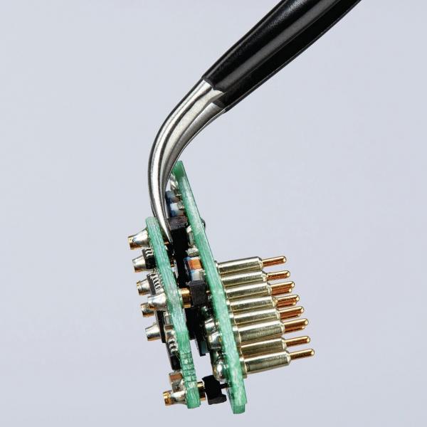 The image shows a circuit board with various golden connectors. A tool is holding the board while the surface is green. The background is bright and neutral.
