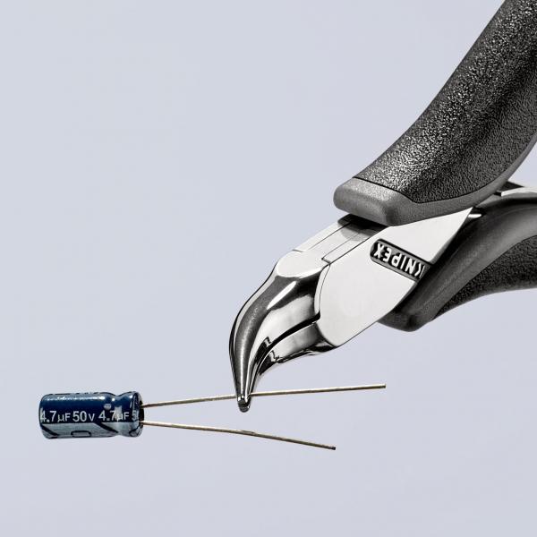 The image shows a precise pair of pliers with a shiny, pointed head holding a blue capacitor with two wire leads in front of it. The background is bright and minimalist.
