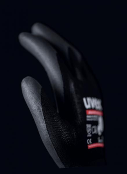 The image shows a black work glove with gray fingers. There is a label on the back of the hand with the text "LIV" and additional information. The background is dark.