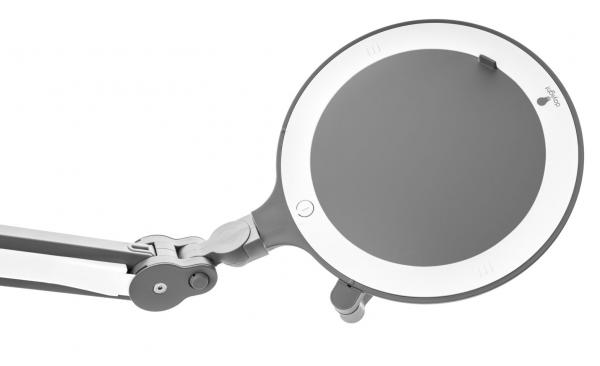Das Bild zeigt eine verstellbare Lupe mit einem runden Glasteil und einem weißen Rand. Sie ist an einem flexiblen Arm befestigt, der zur Anpassung der Position dient.
