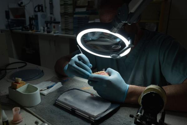 Eine Person trägt Handschuhe und arbeitet unter einer vergrößernden Lampe. Vor ihr liegt ein bearbeitetes Modell. Der Raum ist gedämpft beleuchtet, um präzises Arbeiten zu ermöglichen.
