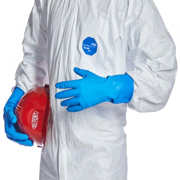 The image shows a person in a white protective suit with blue gloves. In one hand, they hold a red helmet, while the other hand is open.