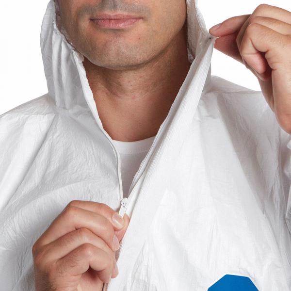 A man puts on a white, lightweight suit with a zipper. He is holding the zipper and stands against a neutral background. Half of his face is visible.
