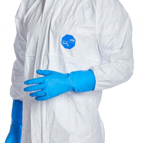 The image shows a human torso in a white protective suit with long sleeves. The left hand is wearing a noticeably blue rubber glove. A blue sticker is visible.