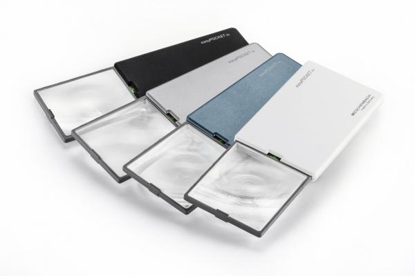 Das Bild zeigt mehrere flache Vergrößerungslinsen in verschiedenen Farben: schwarz, silber, blau und weiß. Sie sind nebeneinander angeordnet, einige sind offen und zeigen die Linse.