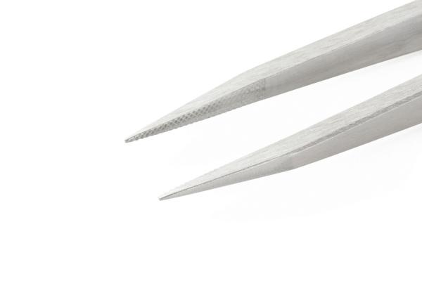 The image shows the tips of a silver tweezer. The tips are narrow and sharp, one is slightly serrated. The background is light and solid-colored.