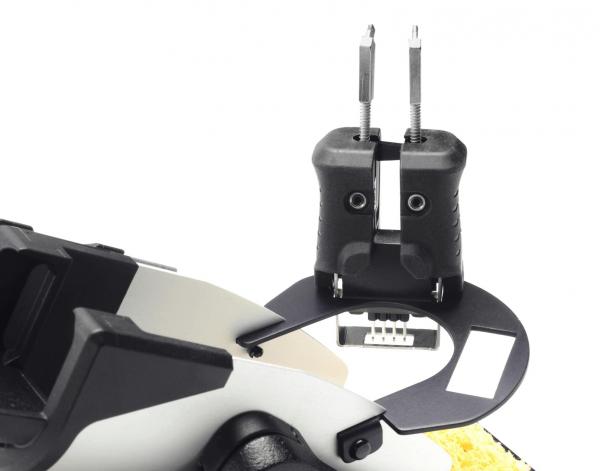 The image displays a technical device with two black handles and a round, flat holder. The holder features a rectangular opening and is equipped with screws.