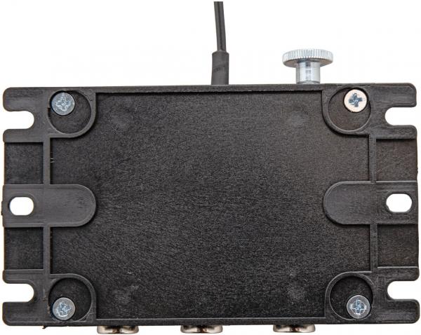 Das Bild zeigt ein flaches, rechteckiges, schwarzes Gerät mit einer leicht strukturierten Oberfläche. An der Oberseite befindet sich ein Kabel und ein Drehknopf. Sechseckige Schrauben sind an den Ecken sichtbar.