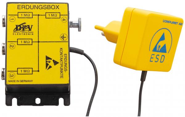 Das Bild zeigt eine gelbe Erdungsbox mit mehreren Anschlüssen und einem Stecker. Auf der Box sind technische Symbole und Beschriftungen. Der Stecker hat ein ESD-Symbol. Alles hat eine technische Funktion.