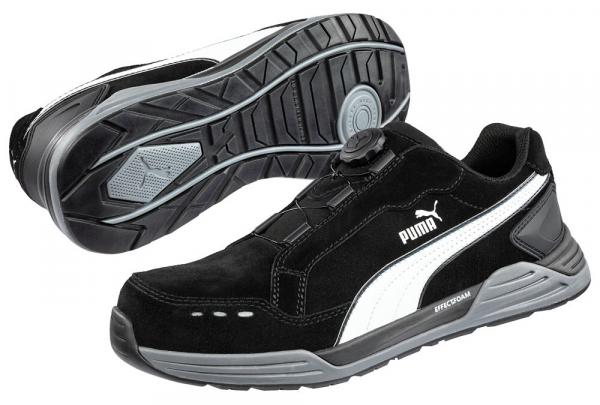 The image shows a black sports shoe with gray and white accents. It features a flat sole with good tread and a unique lacing mechanism instead of traditional laces.