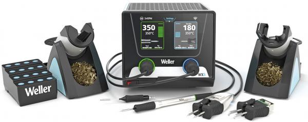 The image shows a soldering station with a digital display in the middle, two soldering tip holders on both sides, a holder for soldering wire, and several cables.