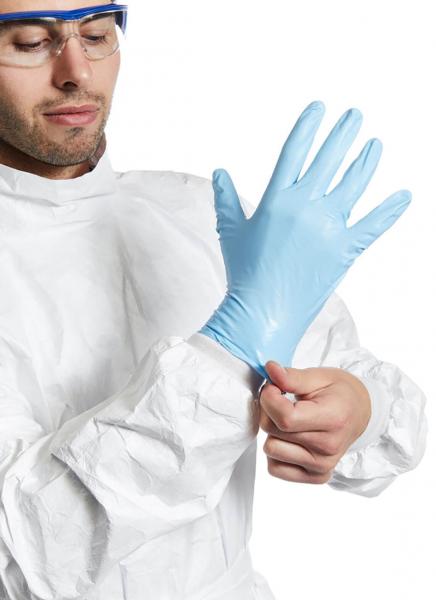 A man in a white protective suit is putting on a blue rubber glove. He is wearing safety goggles and focusing on the task.