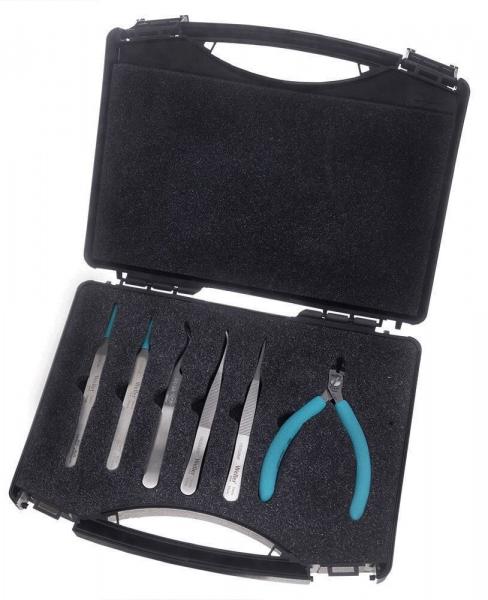 The image displays a black toolset with a folding box. Inside the box, there are six fine tools and a pair of pliers with blue handles. The tools are precise and slim.