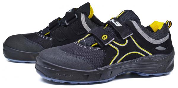 Das Bild zeigt ein Paar sportliche Schuhe. Sie sind überwiegend schwarz mit grauen und gelben Akzenten. Die Schuhe haben einen robusten, rutschfesten Sohle und einen praktischen Klettverschluss.