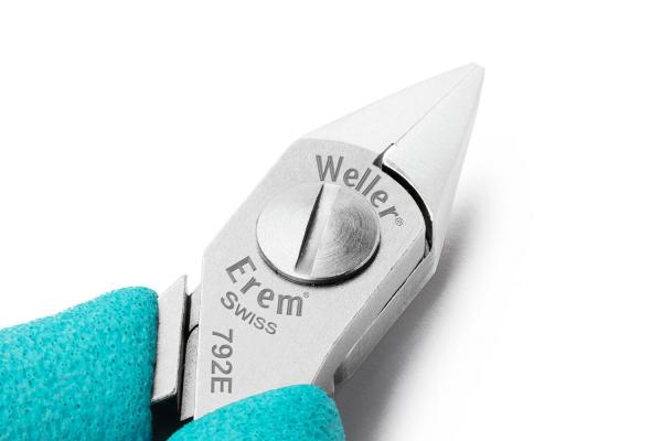 Das Bild zeigt eine spitze Zange mit glattem, glänzendem Metallkopf und einem drehbaren Bedienelement in der Mitte. Der Griff ist hellblau und ergonomisch geformt.