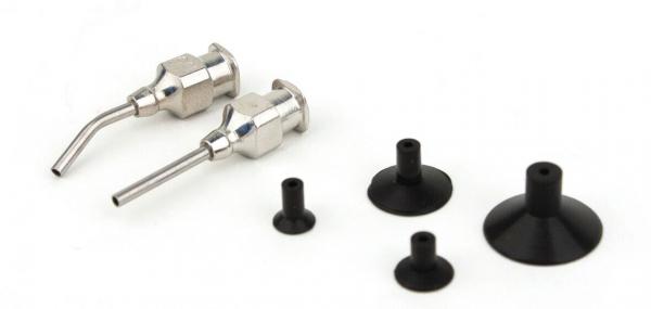 Das Bild zeigt zwei metallische Spritzdüsen neben mehreren gummiartigen, schwarzen Aufsätzen in verschiedenen Größen und Formen. Sie sind auf einer weißen Oberfläche angeordnet.