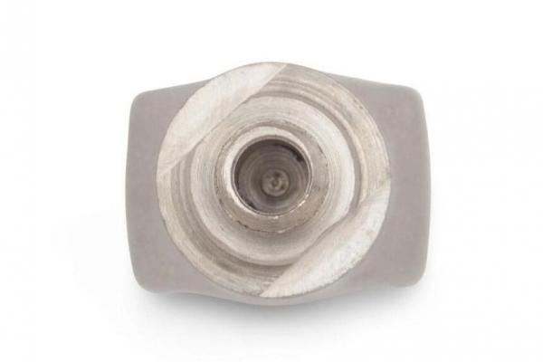 The image shows a silver hexagonal nut lying flat on a bright background. The nut has a central opening and an angled, hexagonal shape.
