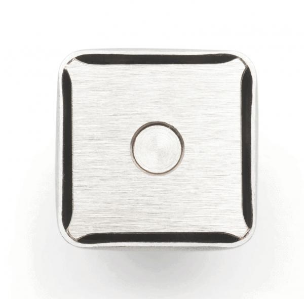 The image shows a square, metallic button. The surface is smooth with a matte texture, and there is a small, round dot in the center. The corners are slightly rounded.