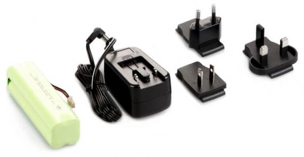 Auf dem Bild sind ein grünes Batteriemodul, ein schwarzes Ladegerät mit Kabel und drei verschiedene Steckeradapter zu sehen. Die Adapter sind in unterschiedlichen Formen gestaltet.