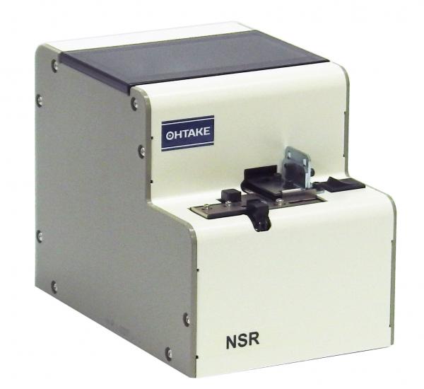 The image shows a compact, rectangular device in white with a black top part. On the front, there are two openings and a folding mechanism. The device features the logo "OHTAKE" and the model name "NSR".
