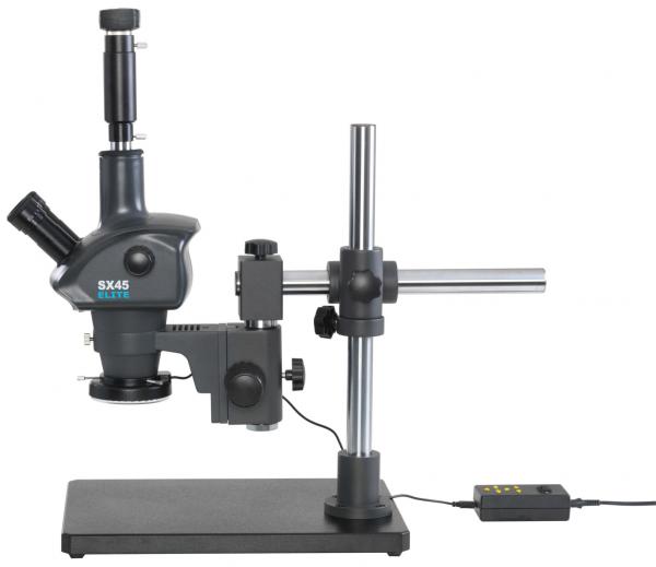 The image shows a microscope with a stable, black base. It has a telescope-like lens, a lateral eyepiece, and a vertical mount that supports the work area. A cable terminates in a control unit.