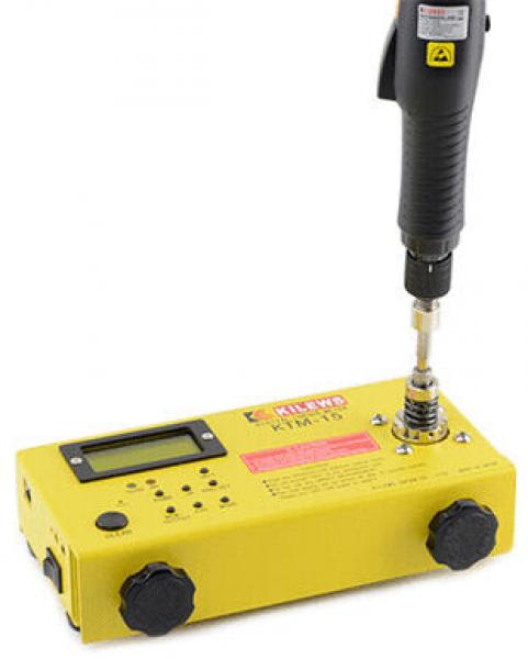 The image shows a yellow, rectangular device with several buttons and a display. At the top is a black handle with a rotating mechanism, indicating its use.