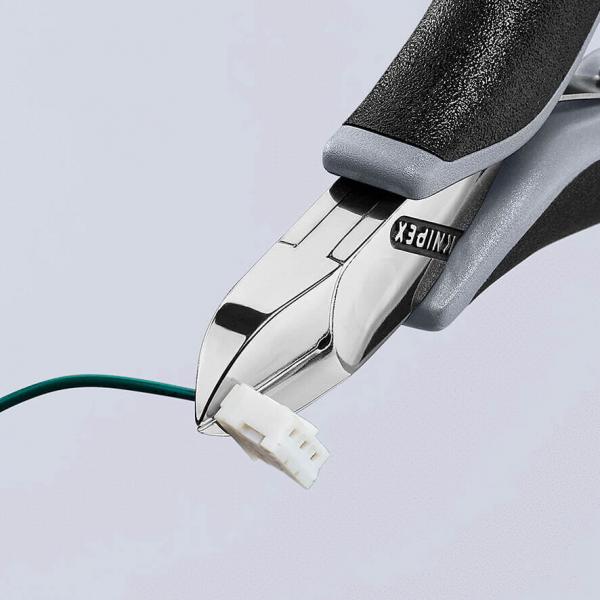 The image shows a pair of pliers gripping a green wire with a white plug. The pliers have black, rubberized handles and a shiny, metallic blade.