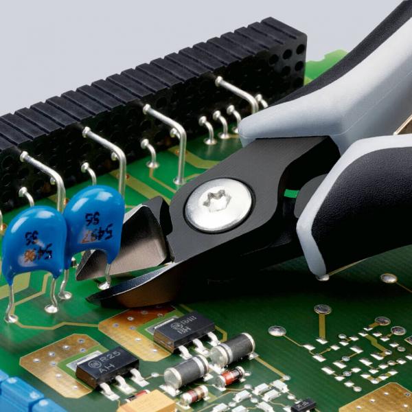 Das Bild zeigt eine Platine mit elektronischen Bauteilen und einer Zange, die gerade einen Draht oder ein Bauteil schneidet. Blau leuchtende Bauelemente sind gut sichtbar.